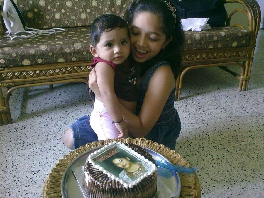 Aadya as a child holding baby Aadi next to a birthday cake.