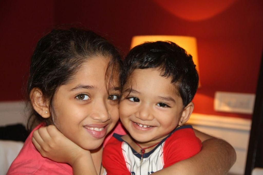Aadya and her brother Aadi as children, cheek to cheek and smiling.