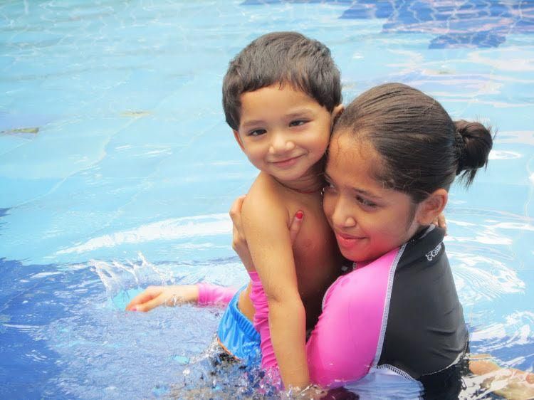 Aadya hugging a young Aadi in a swimming pool.