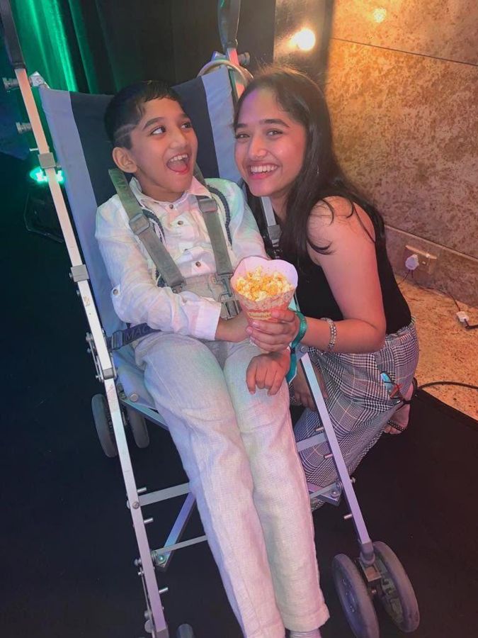 Aadi in his wheelchair at a party, holding popcorn, with Aadya beside him.